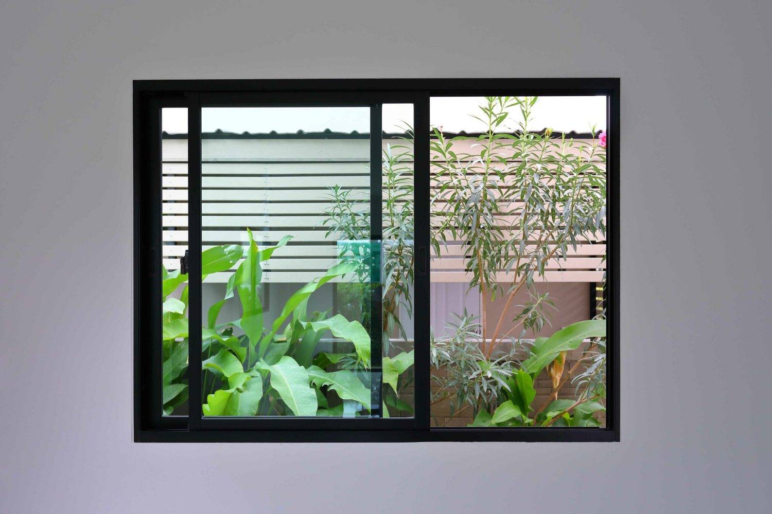 Black aluminum sliding windows in a modern home, overlooking a lush green garden.