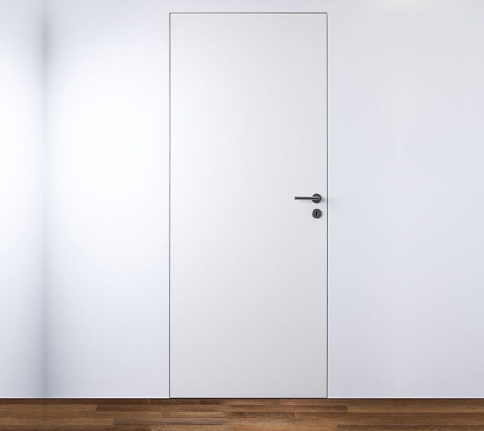 Minimalist modern white interior door with a flush design and sleek black handle, seamlessly blending into a contemporary white wall.