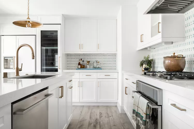 Bright family kitchen mixing stainless appliances with warm gold cabinet hardware, balanced through repeated metal accents and simple white cabinetry.